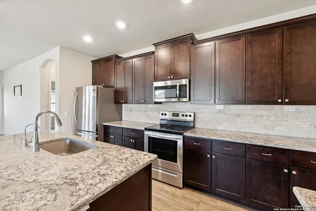 a kitchen with stainless steel appliances granite countertop a sink stove refrigerator and cabinets