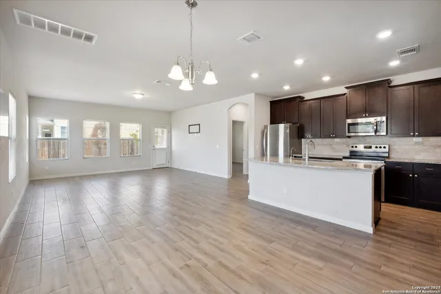 a view of an empty room and kitchen with wooden floor