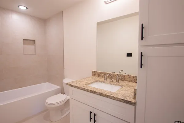 a bathroom with a granite countertop sink a toilet a mirror and bathtub