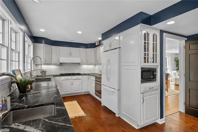 a kitchen with stainless steel appliances granite countertop a refrigerator a sink dishwasher a stove and white cabinets with wooden floor