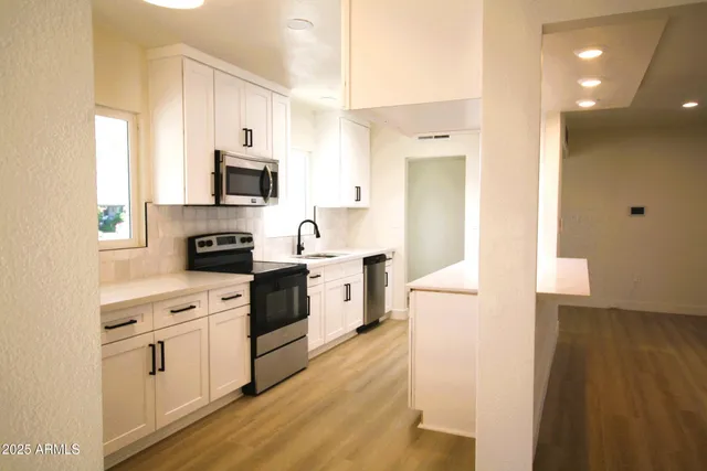 a kitchen with stainless steel appliances a stove top oven a sink a refrigerator white cabinets and wooden floor