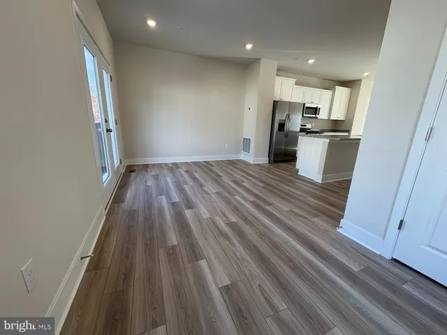 an empty room with wooden floor and a kitchen
