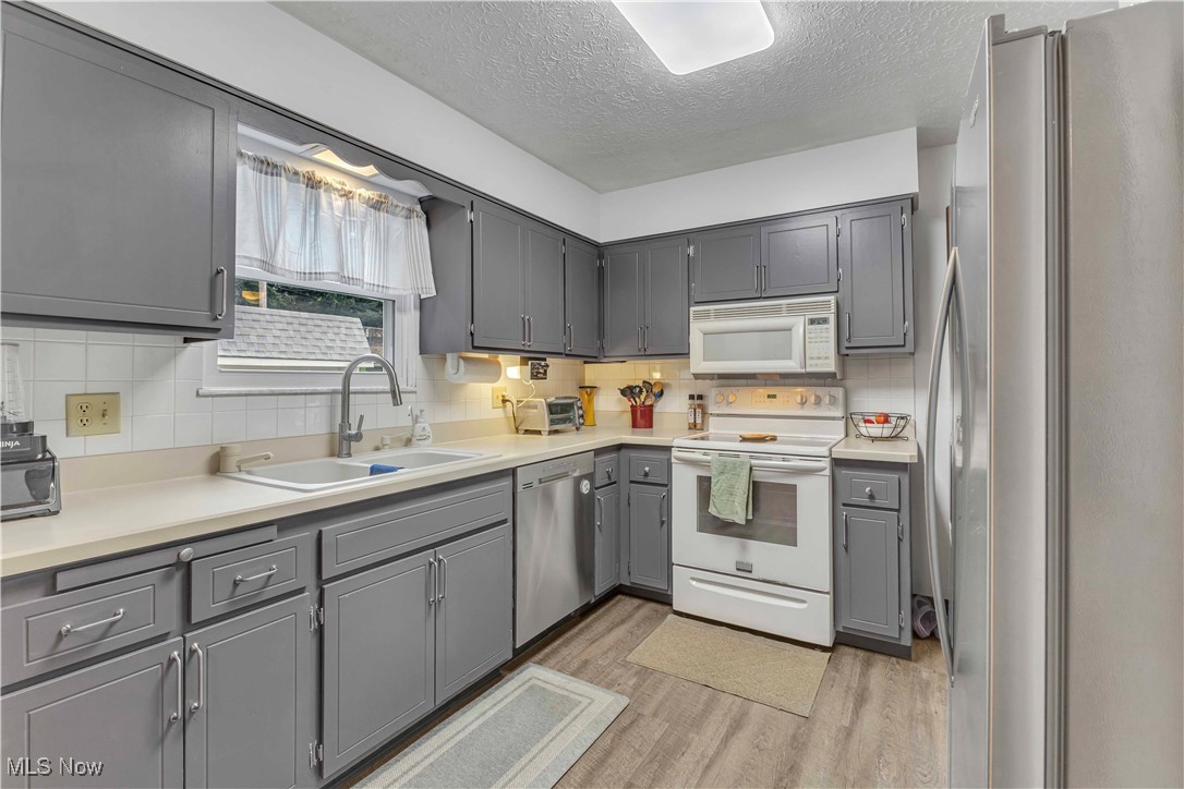 4090 Ridgeview Road Cleveland, OH 44144 - Photo 8 of 40 Kitchen with appliances with stainless steel finishes, gray cabinets, light wood-type flooring, a textured ceiling, and backsplash