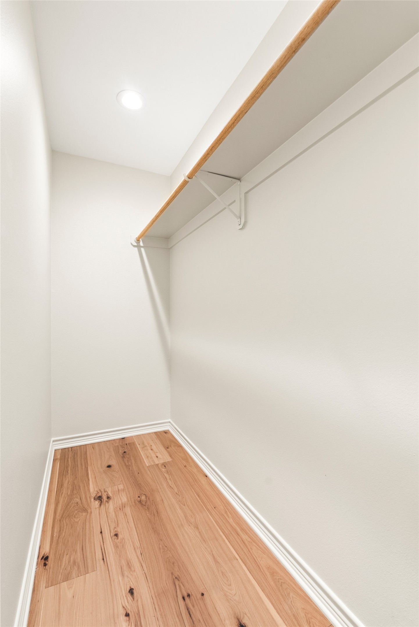 928 Upper Elgin River Road Elgin, TX 78621 - Photo 21 of 40 Walk-in closet with wood-finish flooring, white baseboards, a white built-in shelf, and a natural wood-finish hanging rod.