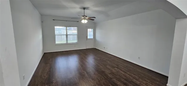 an empty room with wooden floor chandelier fan and windows
