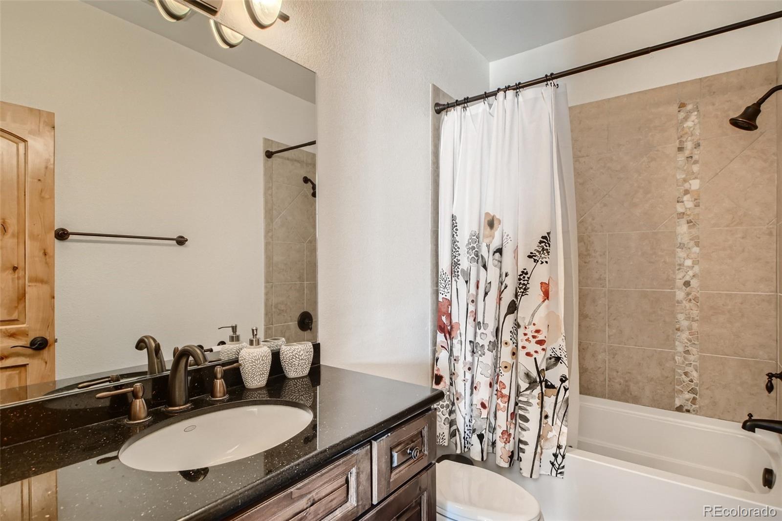 11227 Explorers Run Littleton, CO 80125 - Photo 27 of 33 a bathroom with a granite countertop sink toilet a mirror a shower and a bathtub