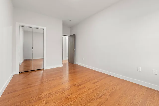 a view of an empty room with wooden floor and closet