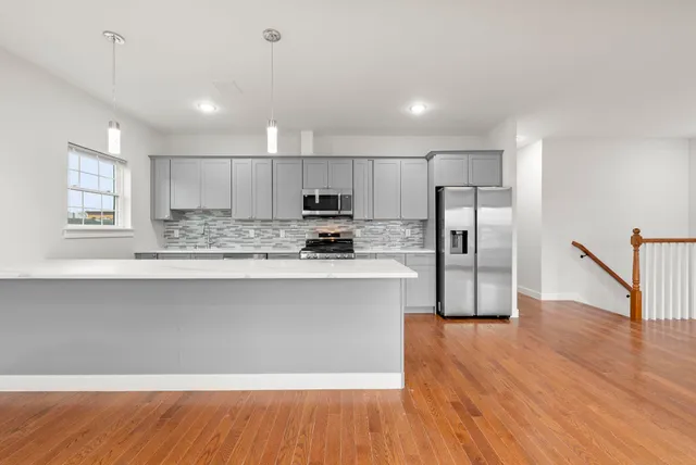 a kitchen with stainless steel appliances granite countertop a refrigerator a sink dishwasher a stove and white cabinets with wooden floor