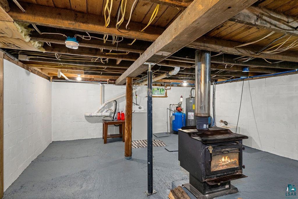 5466 Jean Duluth Road Duluth, MN 55803 - Photo 19 of 34 Basement featuring exposed wood beams, white-painted block walls, a free-standing wood-burning stove, a wall-mounted utility sink, and a water heater