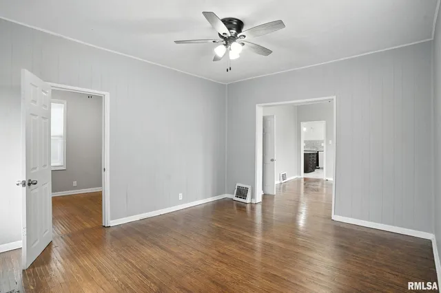 an empty room with wooden floor and a ceiling fan