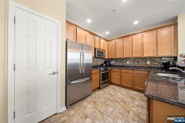 a kitchen with stainless steel appliances granite countertop a refrigerator a sink a stove a washer dryer and a refrigerator