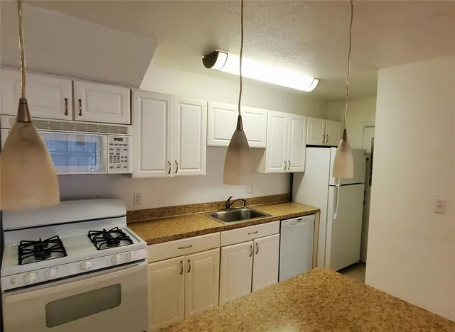 a kitchen with stainless steel appliances granite countertop a sink a stove a refrigerator and white cabinets