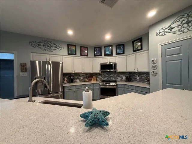 a large kitchen with stainless steel appliances a large counter top a refrigerator a fireplace wooden floor and a couch