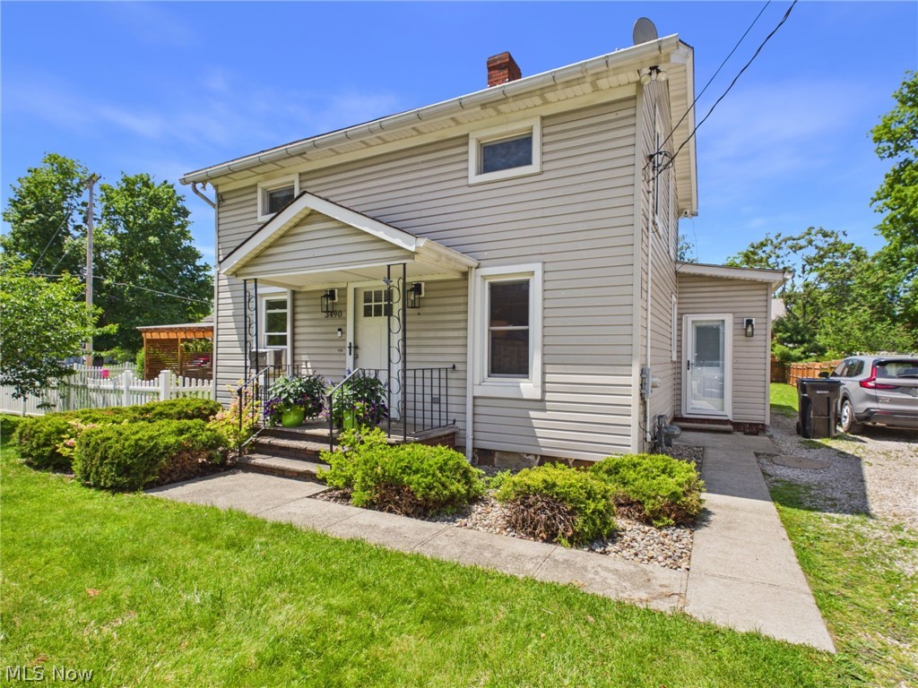 Two-story residence featuring light-colored horizontal siding, a covered front porch with iron railings, and a white picket fence bordering the front yard