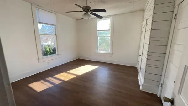 a view of empty room with wooden floor and fan