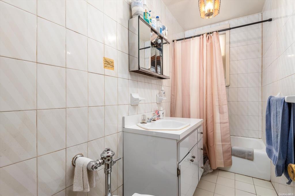 1772 68th Street Brooklyn, NY 11204 - Photo 19 of 34 Bathroom featuring tile walls, shower / tub combo with curtain, vanity, and tile patterned floors
