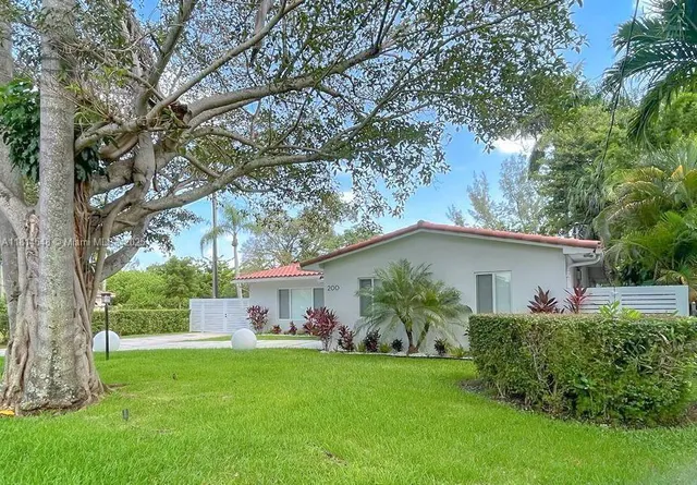 a backyard of a house with table and chairs plants and large tree