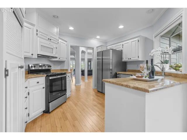 a kitchen with stainless steel appliances sink stove refrigerator and white cabinets with wooden floor