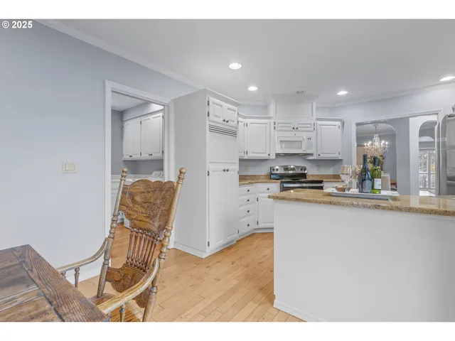 a kitchen with stainless steel appliances kitchen island granite countertop a refrigerator a stove a sink dishwasher and white cabinets with wooden floor