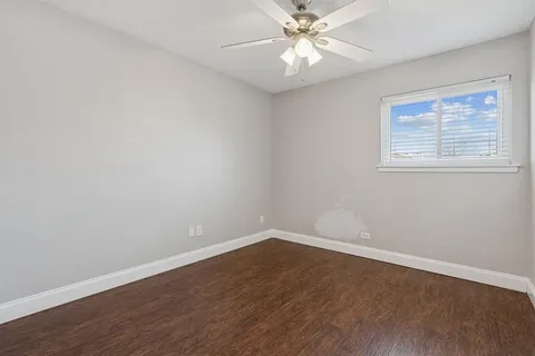 a view of an empty room with wooden floor and a chandelier fan