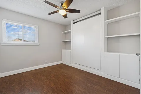 an empty room with wooden floor closet fan and windows