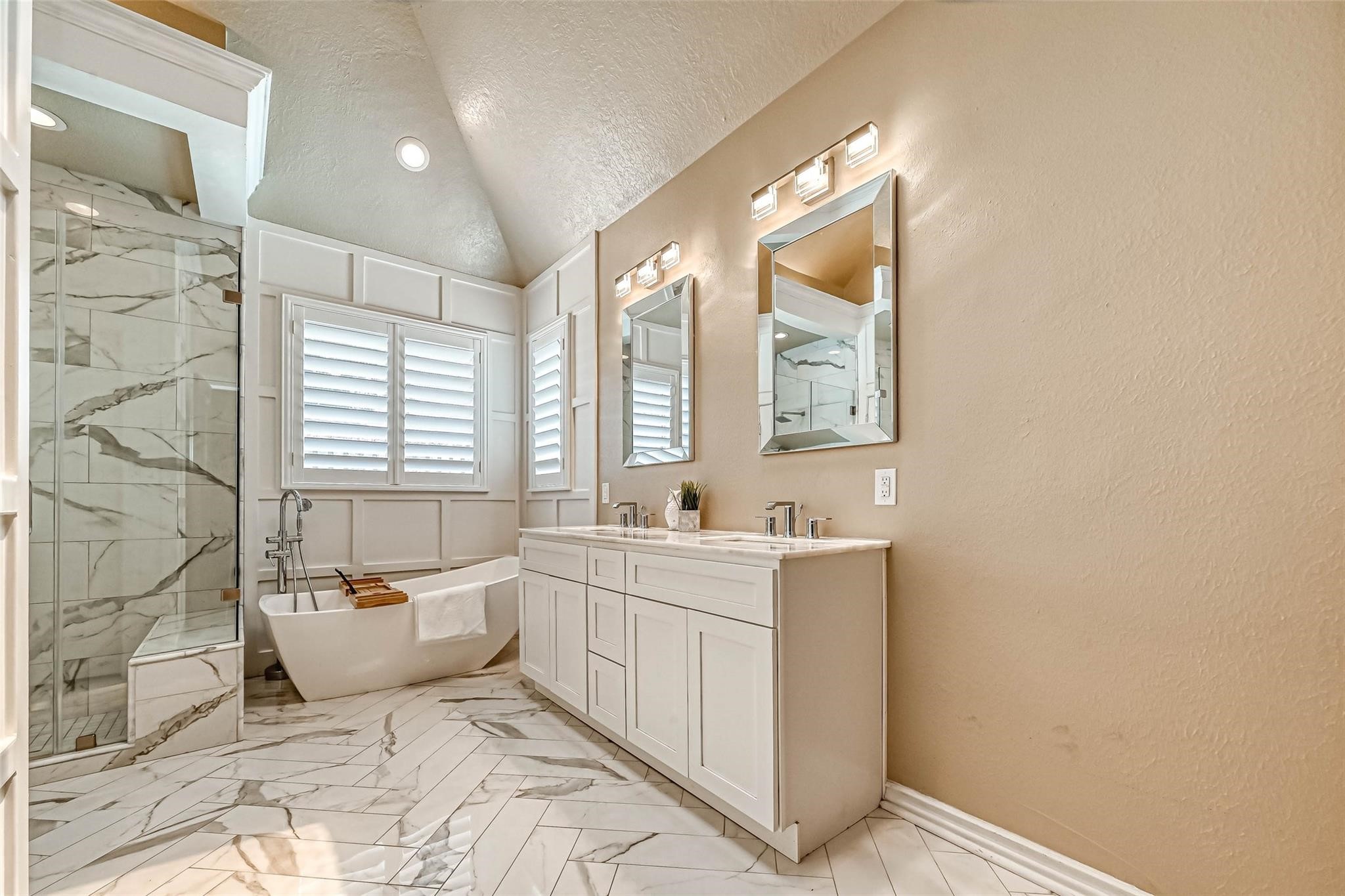 263 Wood Loop Street Houston, TX 77015 - Photo 27 of 45 Bright, elegant bathroom featuring a freestanding tub, glass-enclosed shower with marble accents, and a double vanity with modern fixtures. Natural light streams through stylish shutters, highlighting the spacious, sophisticated design.
