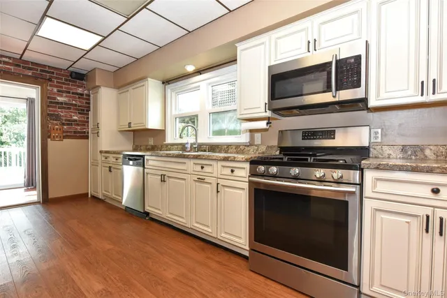 a kitchen with stainless steel appliances white cabinets a sink a stove a microwave and wooden floors