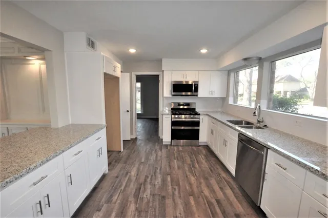 a large kitchen with a center island wooden floor stainless steel appliances and windows
