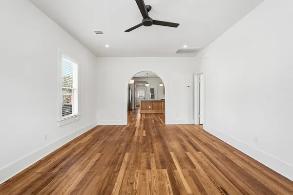 a big room with wooden floor a chandelier fan and windows