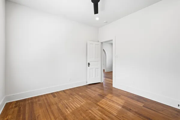 an empty room with wooden floor and a ceiling fan
