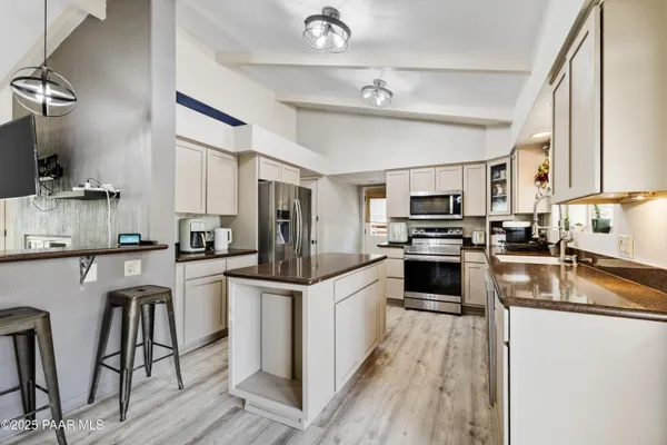 a kitchen with stainless steel appliances granite countertop a refrigerator a stove top oven a sink dishwasher and white cabinets with wooden floor