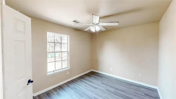an empty room with wooden floor fan and windows