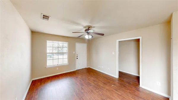 an empty room with wooden floor chandelier fan and windows