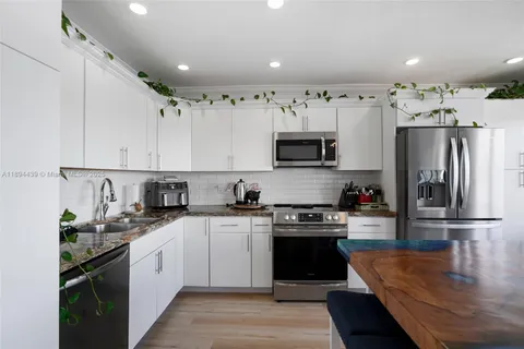 a kitchen with stainless steel appliances granite countertop a refrigerator a sink dishwasher a stove and white cabinets with wooden floor