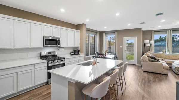 a large white kitchen with granite countertop a stove a sink a dining table and chairs