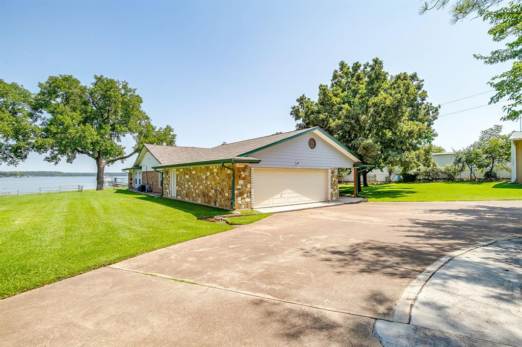 11484 Moran Road Azle, TX 76020 - Photo 4 of 40 View of side of property featuring a yard, concrete driveway, brick siding, a garage, and a water view