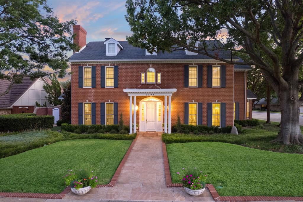 a front view of a house with a yard and potted plants and large trees
