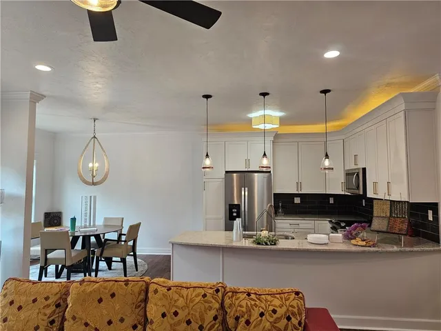 a kitchen with stainless steel appliances kitchen island granite countertop a refrigerator a stove a sink dishwasher and white cabinets with wooden floor