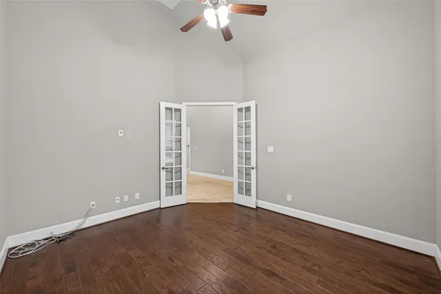 an empty room with wooden floor chandelier fan and windows