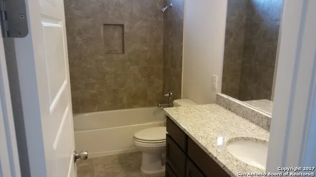 a bathroom with a granite countertop bathtub shower sink vanity and toilet