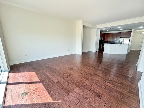 an empty room with wooden floor and kitchen view