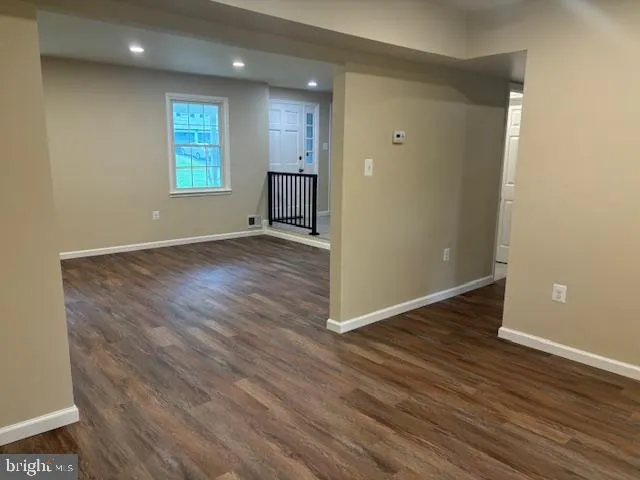 a view of an empty room with wooden floor and a kitchen