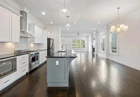 a kitchen with stainless steel appliances granite countertop a stove top oven a sink dishwasher a refrigerator and a dining table with wooden floor