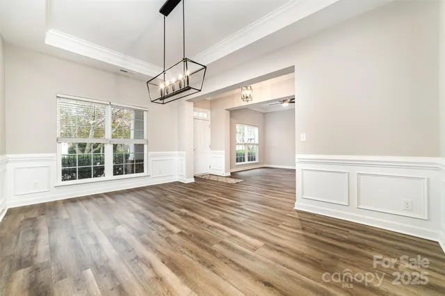 a view of an empty room with wooden floor kitchen view and a window
