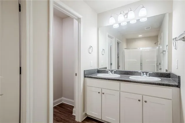 a bathroom with a granite countertop double vanity sink a mirror and a shower