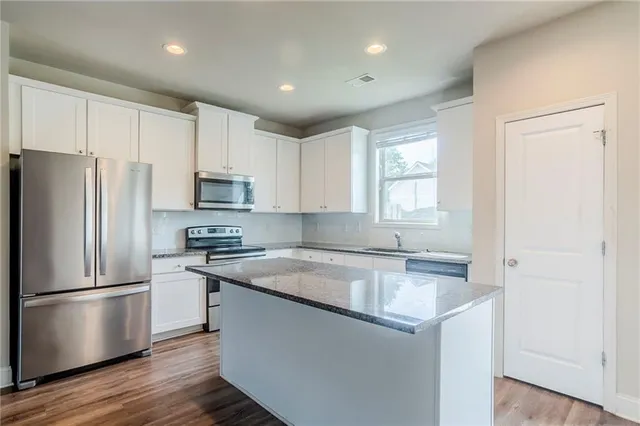 a kitchen with stainless steel appliances granite countertop a refrigerator a sink dishwasher a stove and white countertops with wooden floor