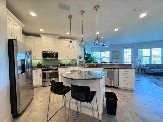 a kitchen with stainless steel appliances kitchen island granite countertop a sink a stove a refrigerator and chairs