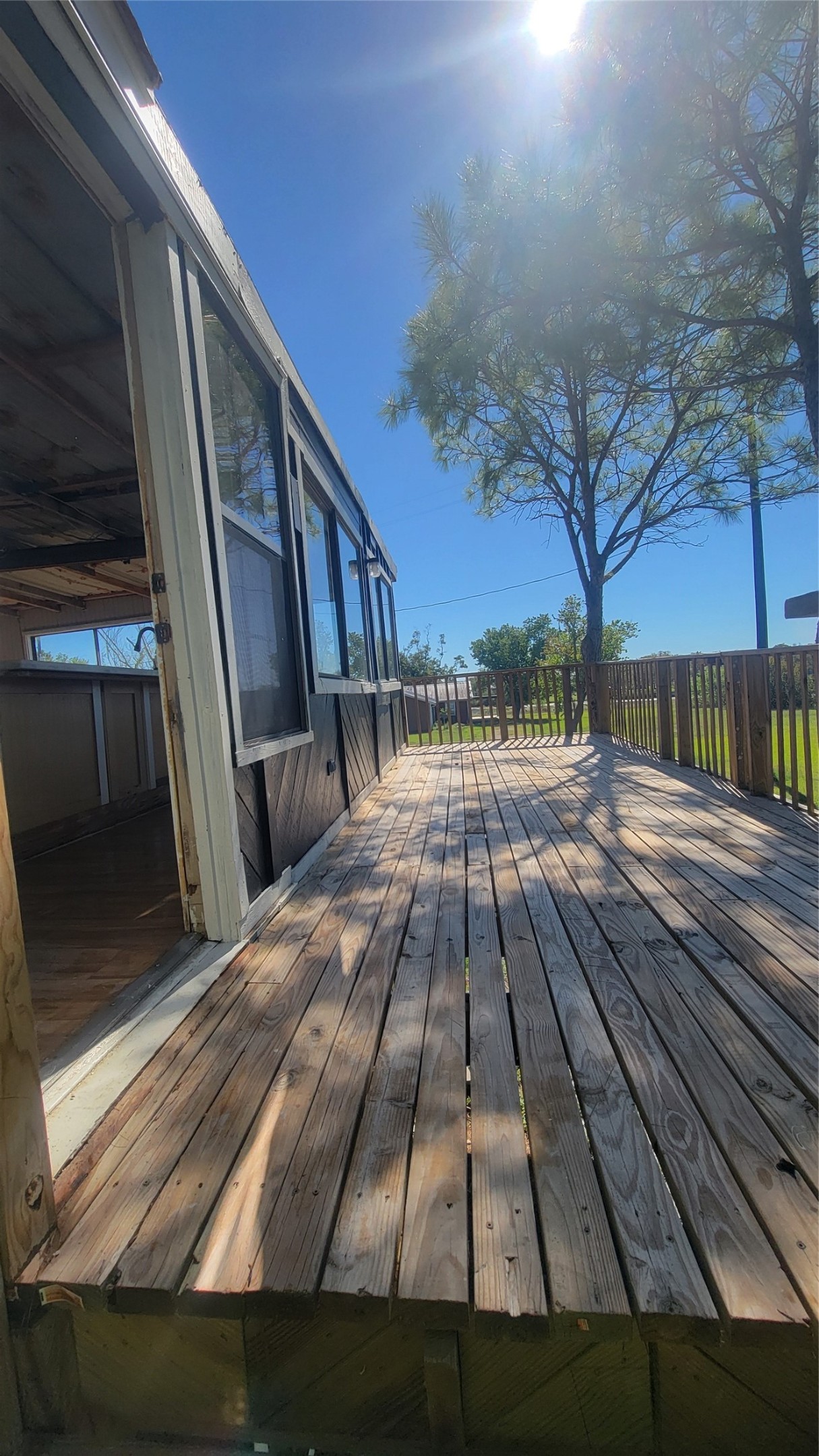 12018 Sandpiper Road Angleton, TX 77515 - Photo 5 of 48 This photo features a wooden deck attached to a home, partially enclosed with large windows, offering a bright outdoor space with tree shade and railing. Ideal for relaxation or entertaining, it provides a seamless indoor-outdoor transition.