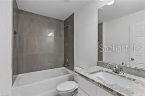 a bathroom with a granite countertop bathtub shower sink vanity mirror and toilet