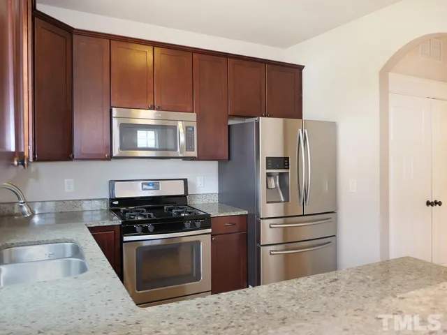 a kitchen with granite countertop wooden cabinets a refrigerator stove and microwave